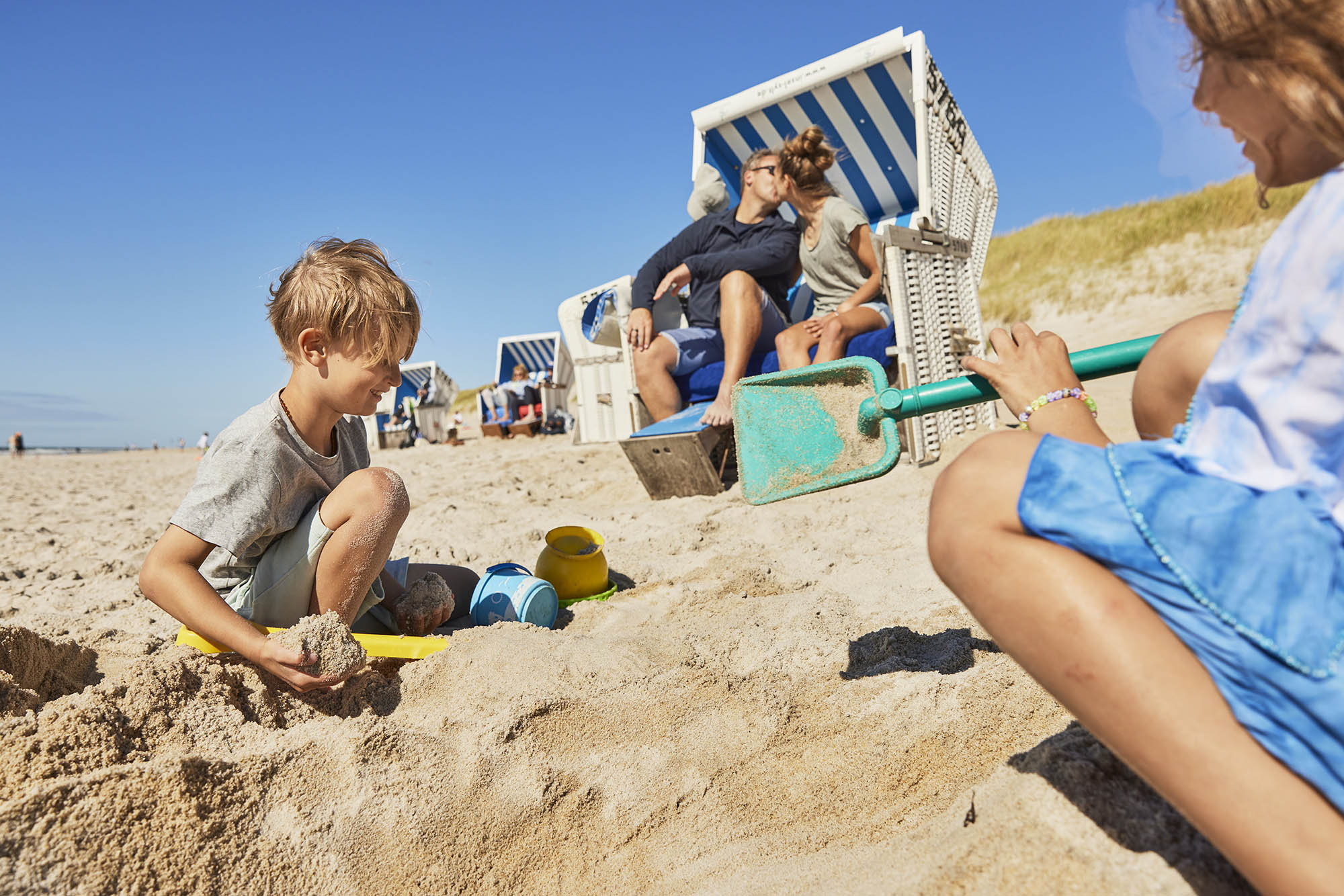 Mann und Frau sitzen küssend im Strandkorb am Westerländer Strand, Mädchen und Junge spielen davor im Sand