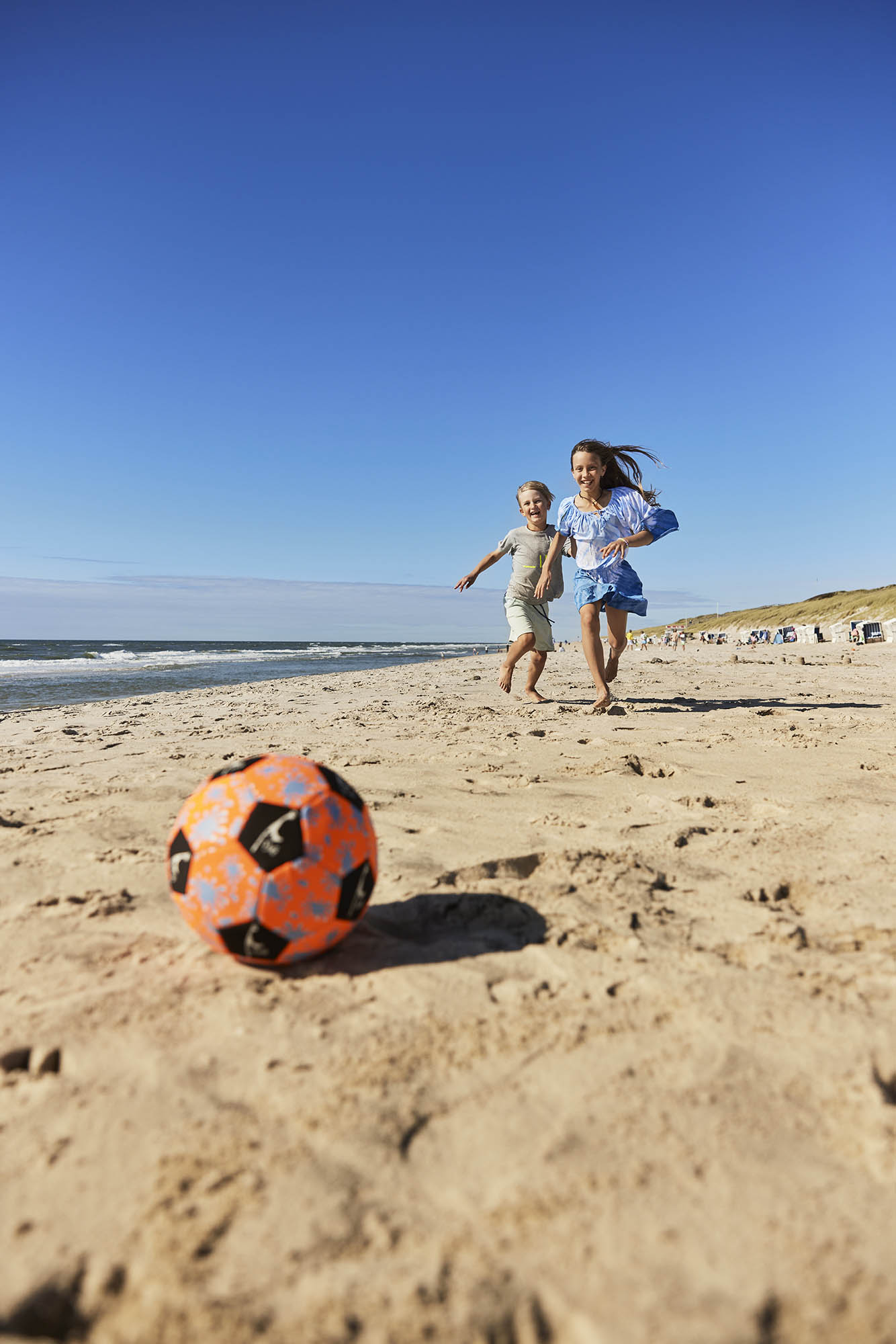 Junge und Mädchen jagen einem Fußball am Strand hinterher