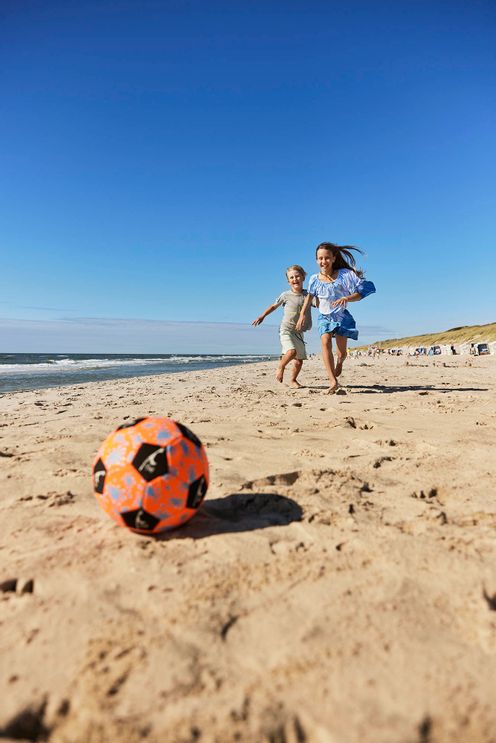 Junge und Mädchen jagen einem Fußball am Strand hinterher