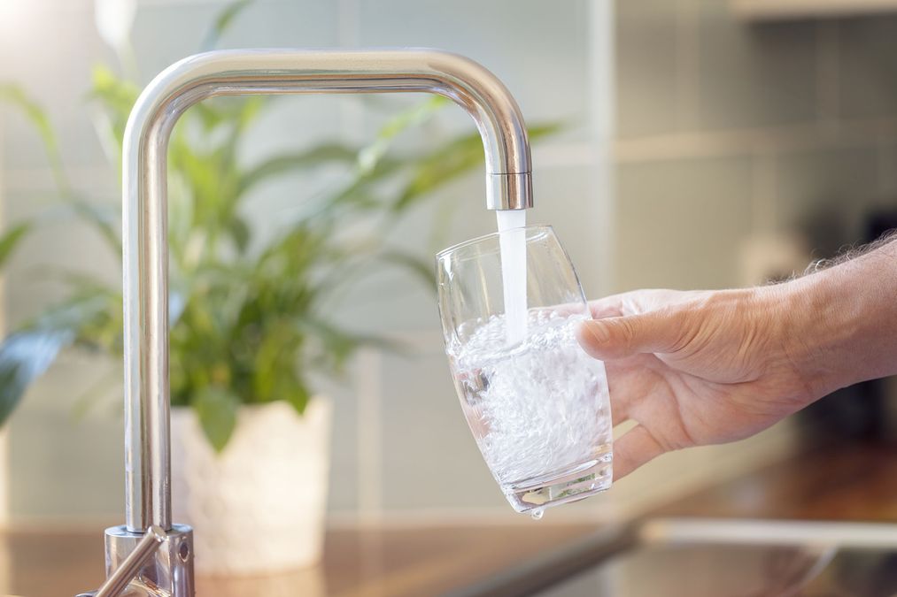 Person lässt Wasser auf Wasserhahn in Glas laufen