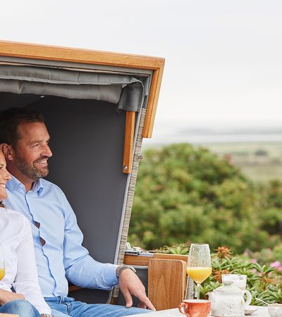 Frau und Mann sitzen im Strandkorb und trinken Orangensaft und Tee