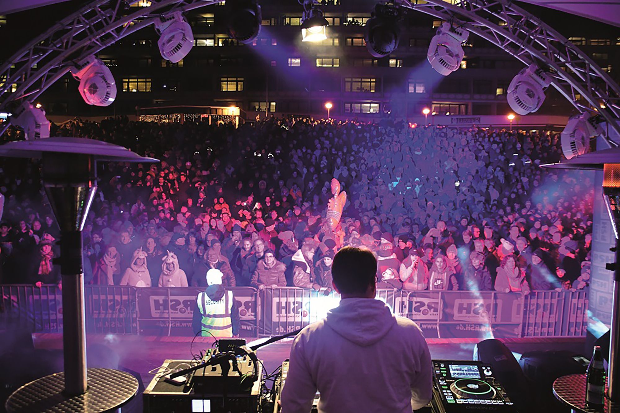 DJ steht in der Musikmuschel vor großem feiernden Publikum