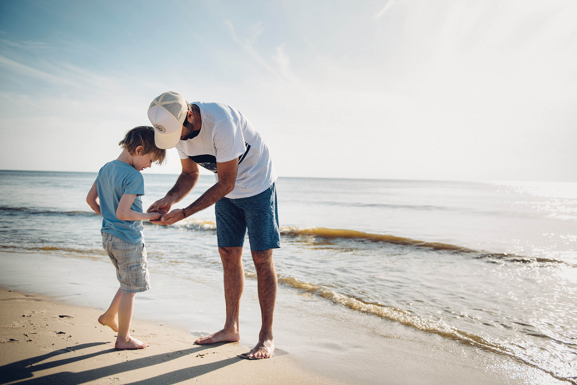 Mann schaut in die Hand eines Jungen am Flutsaum der Nordsee vor Sylt
