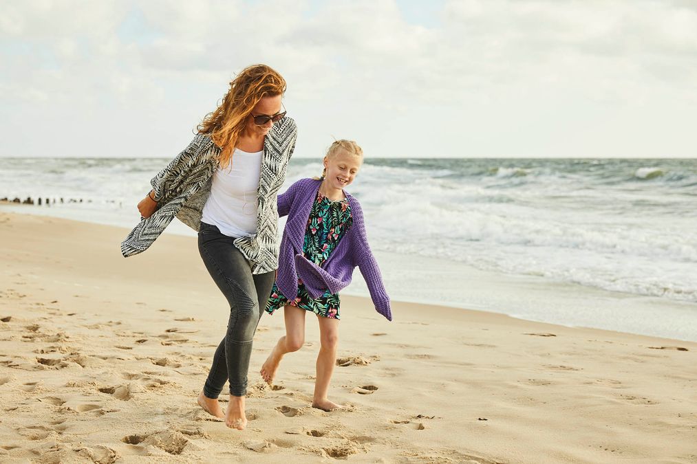 Frau und Mädchen laufen Hand in Hand am Flutsaum der Nordsee