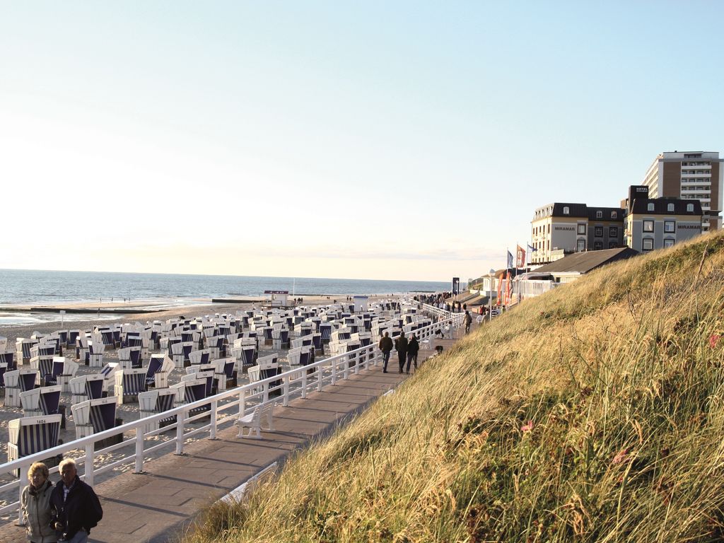 Menschen spazieren auf der Strandpromenade von Westerland, Strandkörbe und das Kurzentrum im Hintergrund