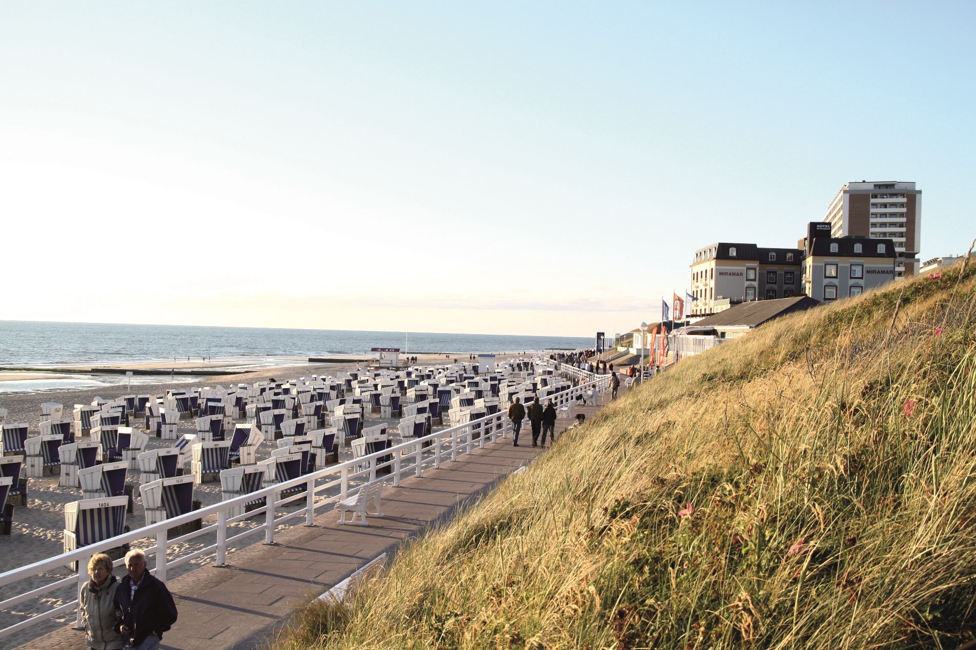 Menschen spazieren auf der Strandpromenade von Westerland, Strandkörbe und das Kurzentrum im Hintergrund