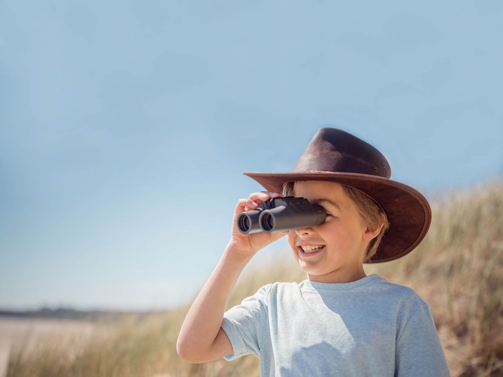 Mädchen in Entdeckeroutfit schaut durch Fernglas