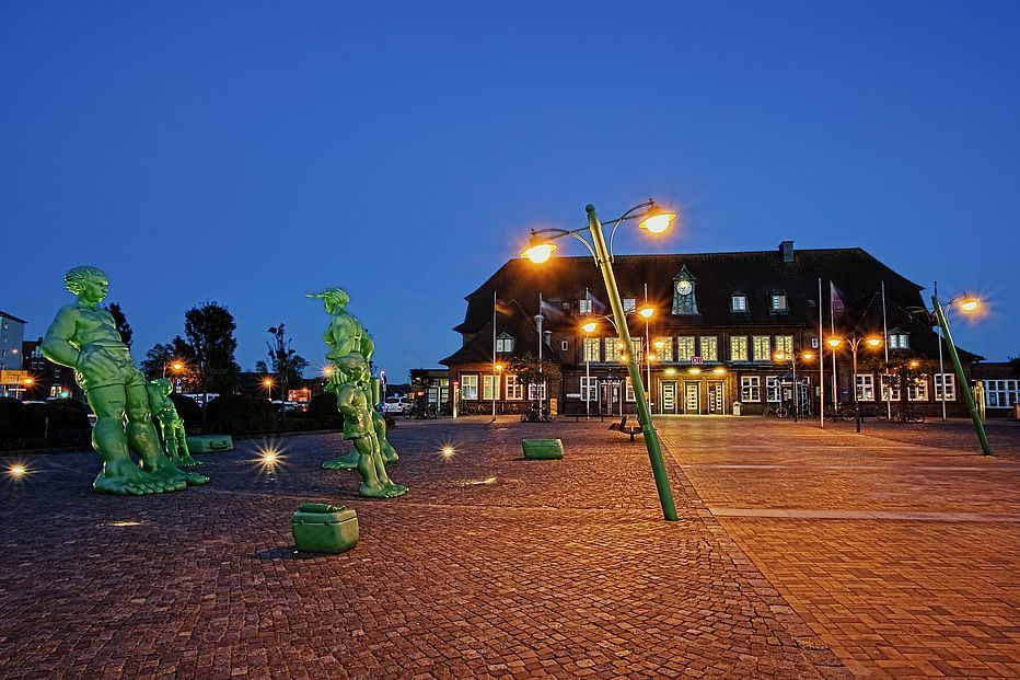 Bahnhofsgebaeude Westerland mit Bahnhofsvorplatz und gruenen Skulpturen, Abendstimmung mit Beleuchtung