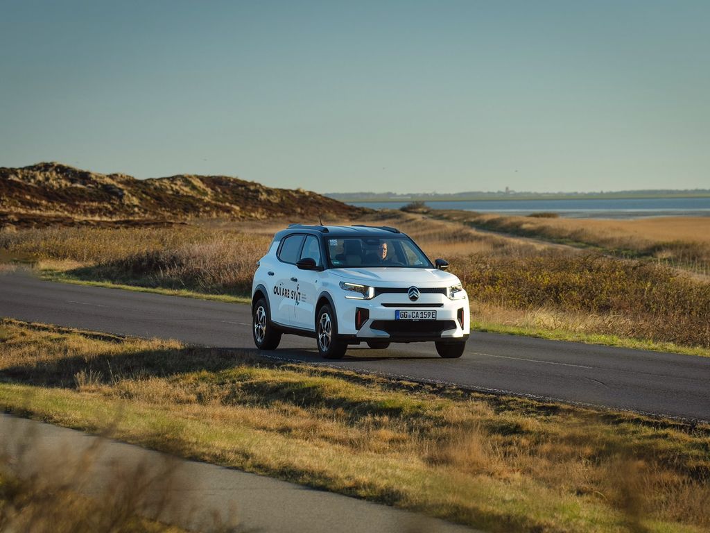 E-Auto C3 von Citroën unterwegs auf Sylter Straßen mit dem Wattenmeer und der Keitumer Kirche im Hintergrund