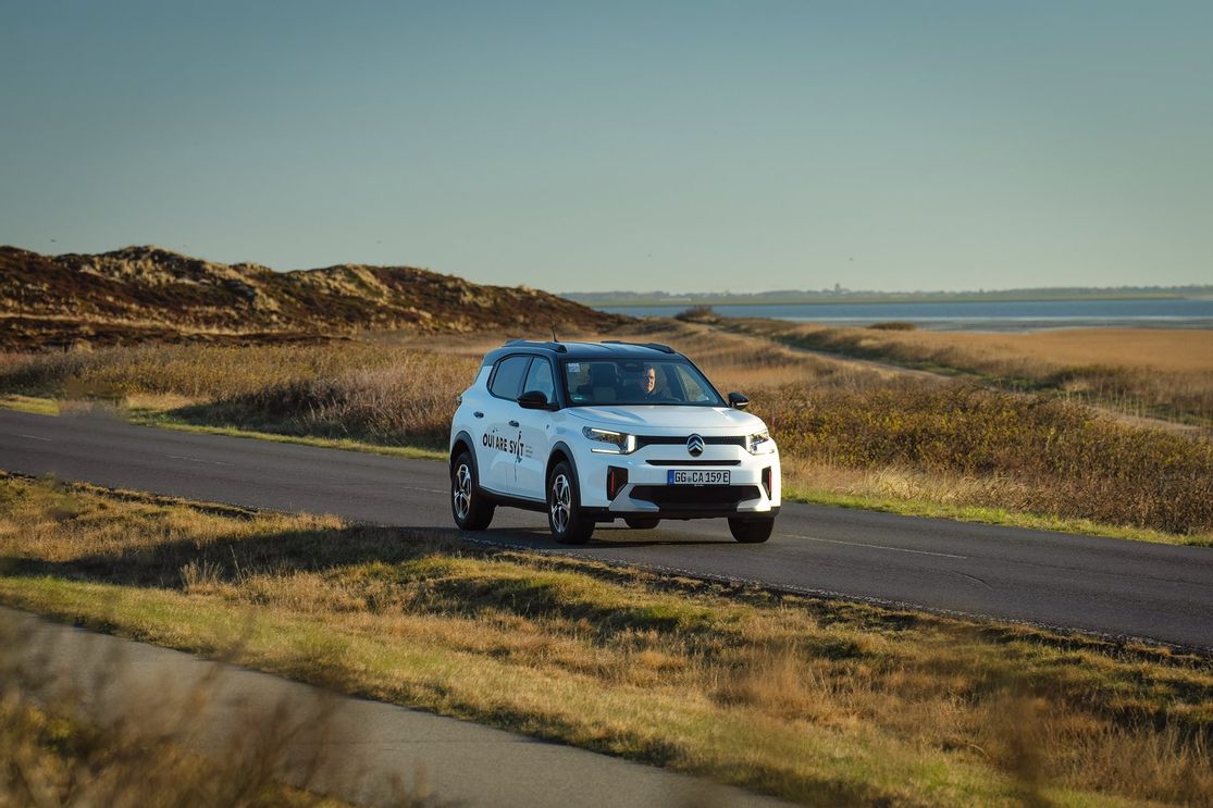 E-Auto C3 von Citroën unterwegs auf Sylter Straßen mit dem Wattenmeer und der Keitumer Kirche im Hintergrund