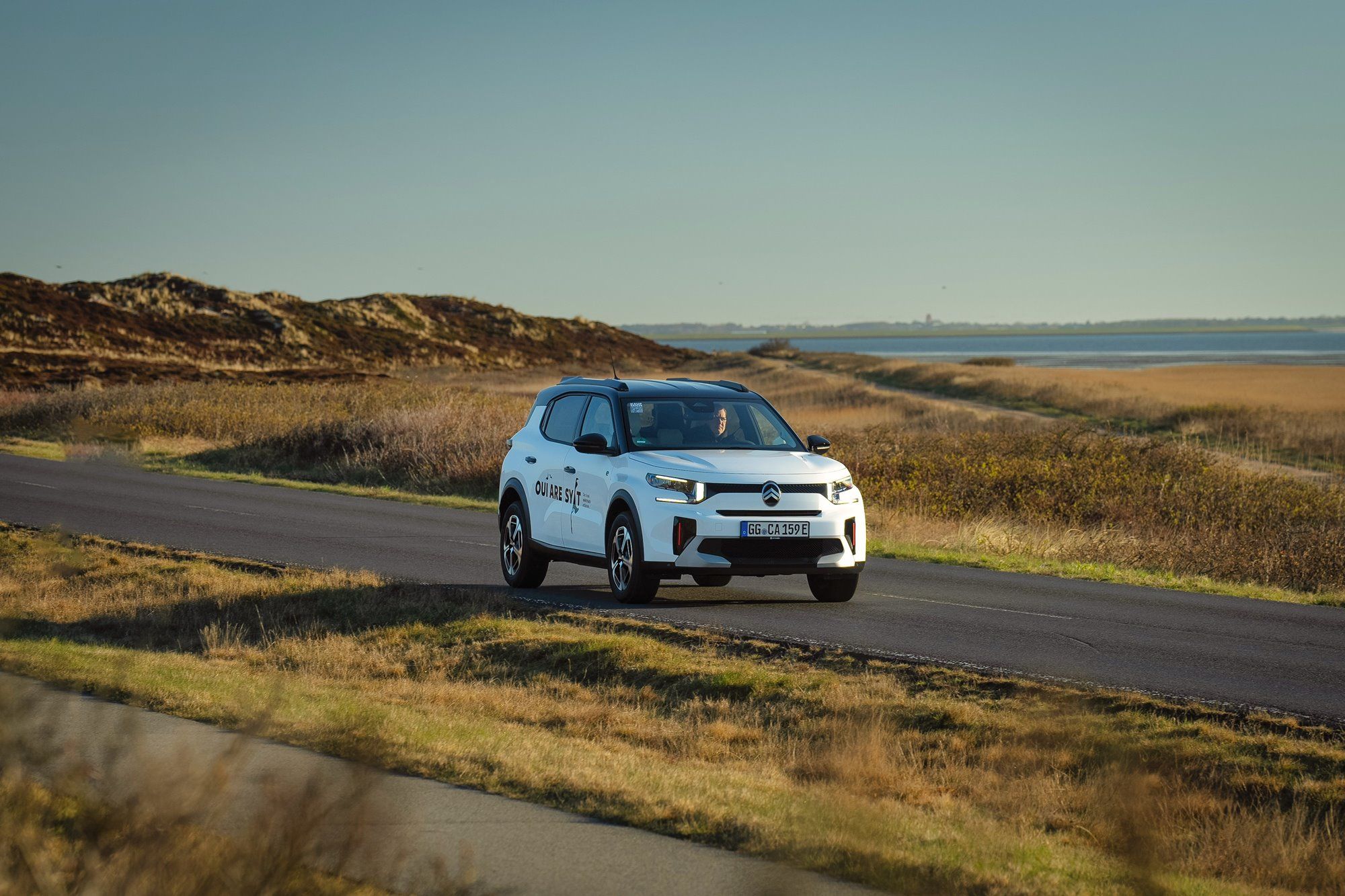 E-Auto C3 von Citroën unterwegs auf Sylter Straßen mit dem Wattenmeer und der Keitumer Kirche im Hintergrund