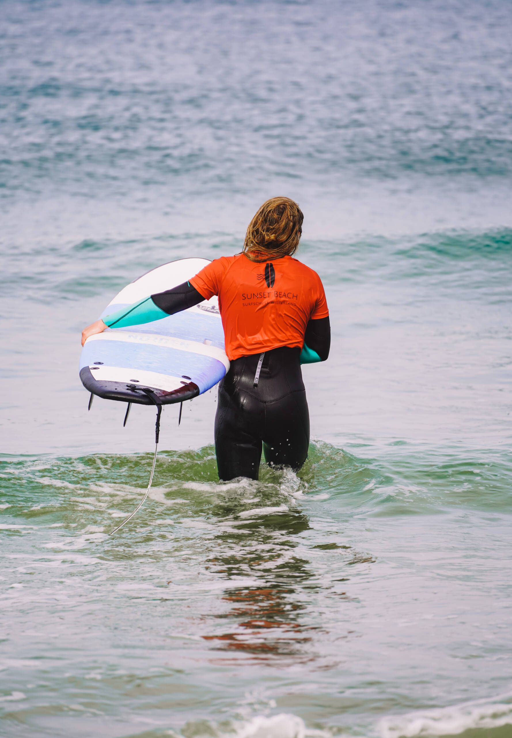 Mann im Meer mit einem Surfbrett in der Hand.