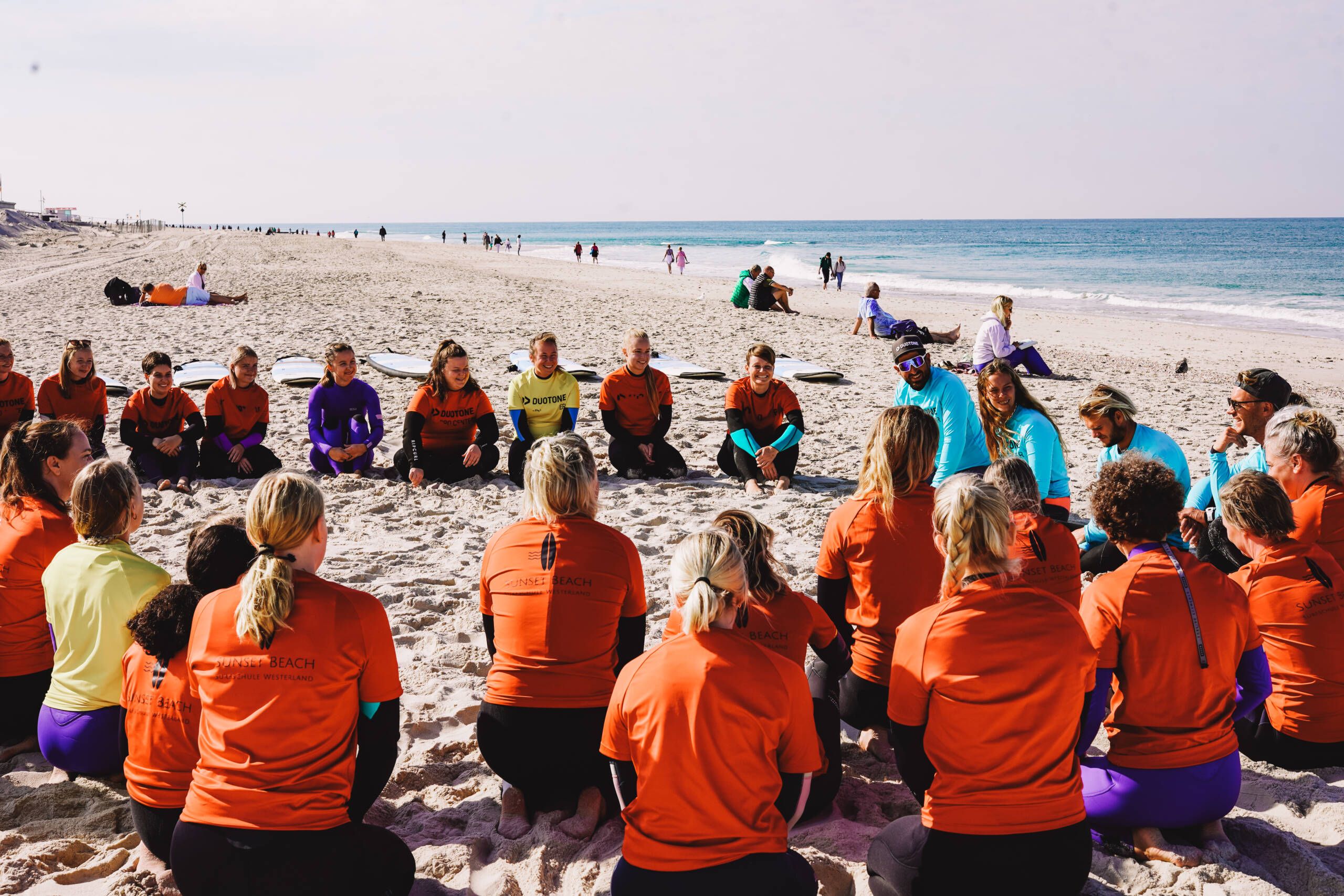 Surfschüler, die im Sand im Kreis sitzen.