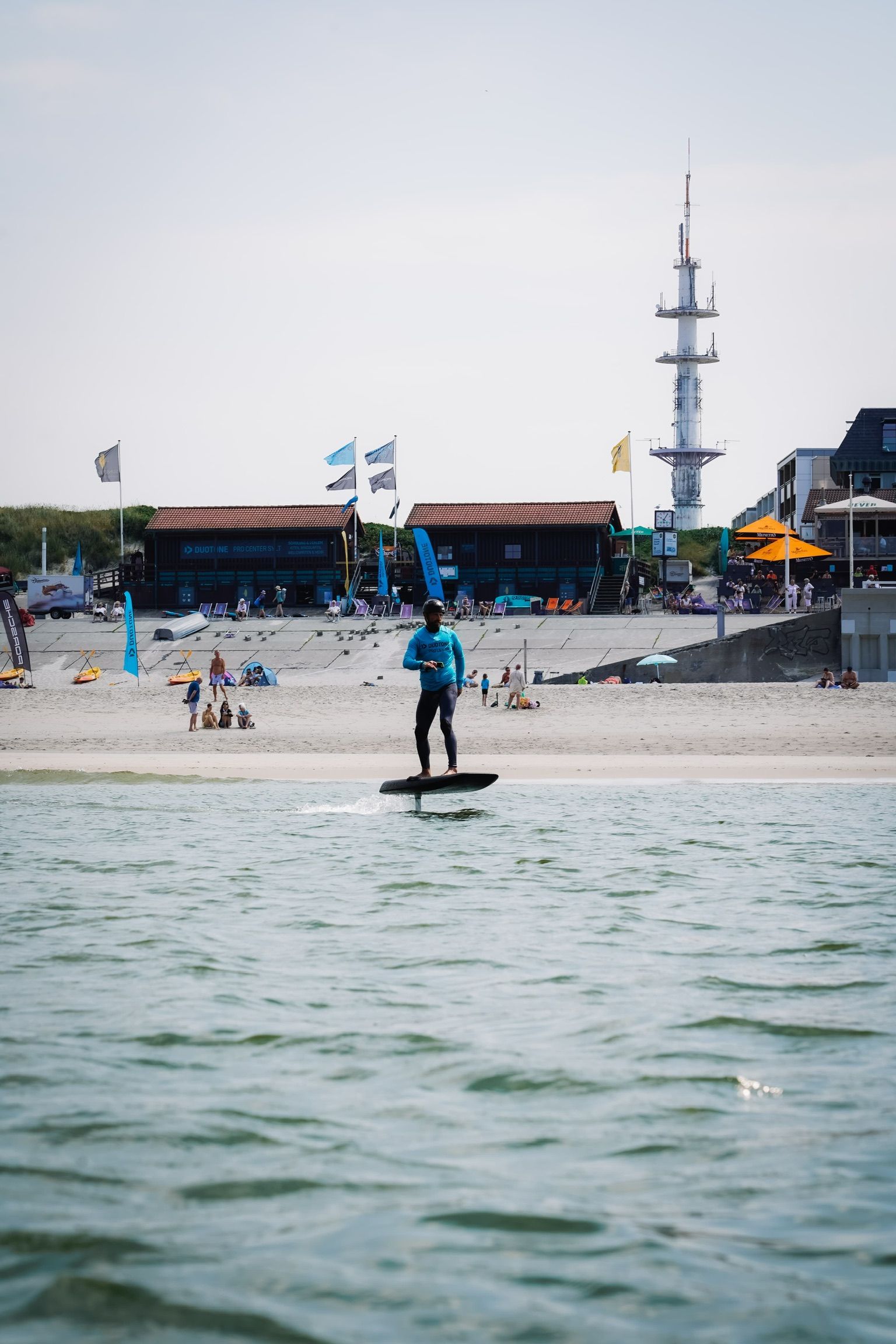Mann auf einem Efoiling Board mit der Surfschule im Hintergrund.