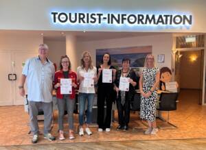 Sechs Mitarbeiter der Tourist-Informationen des Insel Sylt Tourismus-Service freuen sich über die neue Zertifizierung des DTV und halten die entsprechenden Urkunden hoch.