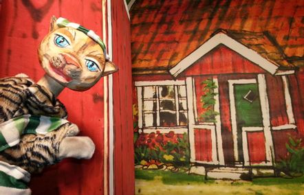 Eine Katzenfigur namens Findus steht vor einem Bild von einem roten Holzhaus.