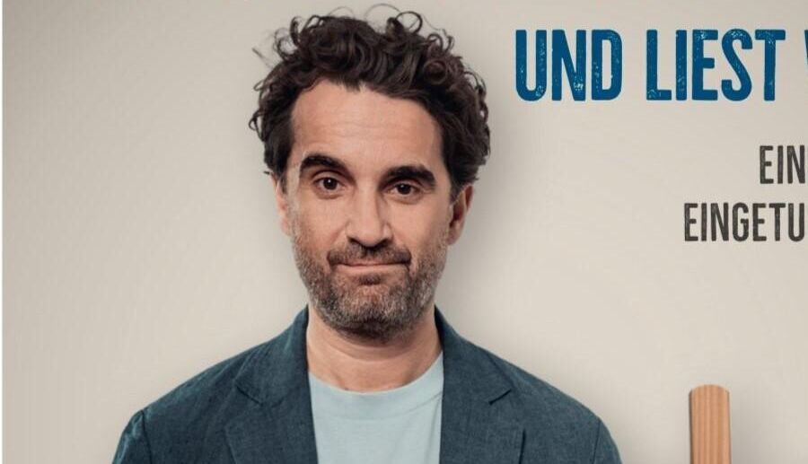 Oliver Wnuk vor grauer Wand, darüber in großer Schrift der Name seines Programms: Wnuk denkt laut und liest was vor. Eine biographisch eingetunkte Leseshow, wobei Lese durchgestrichen ist