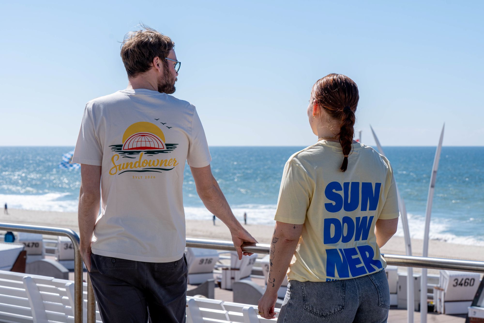 Ein Mann und eine Frau stehen vor der Musikmuschel und tragen die Sundowner T-Shirts 2026