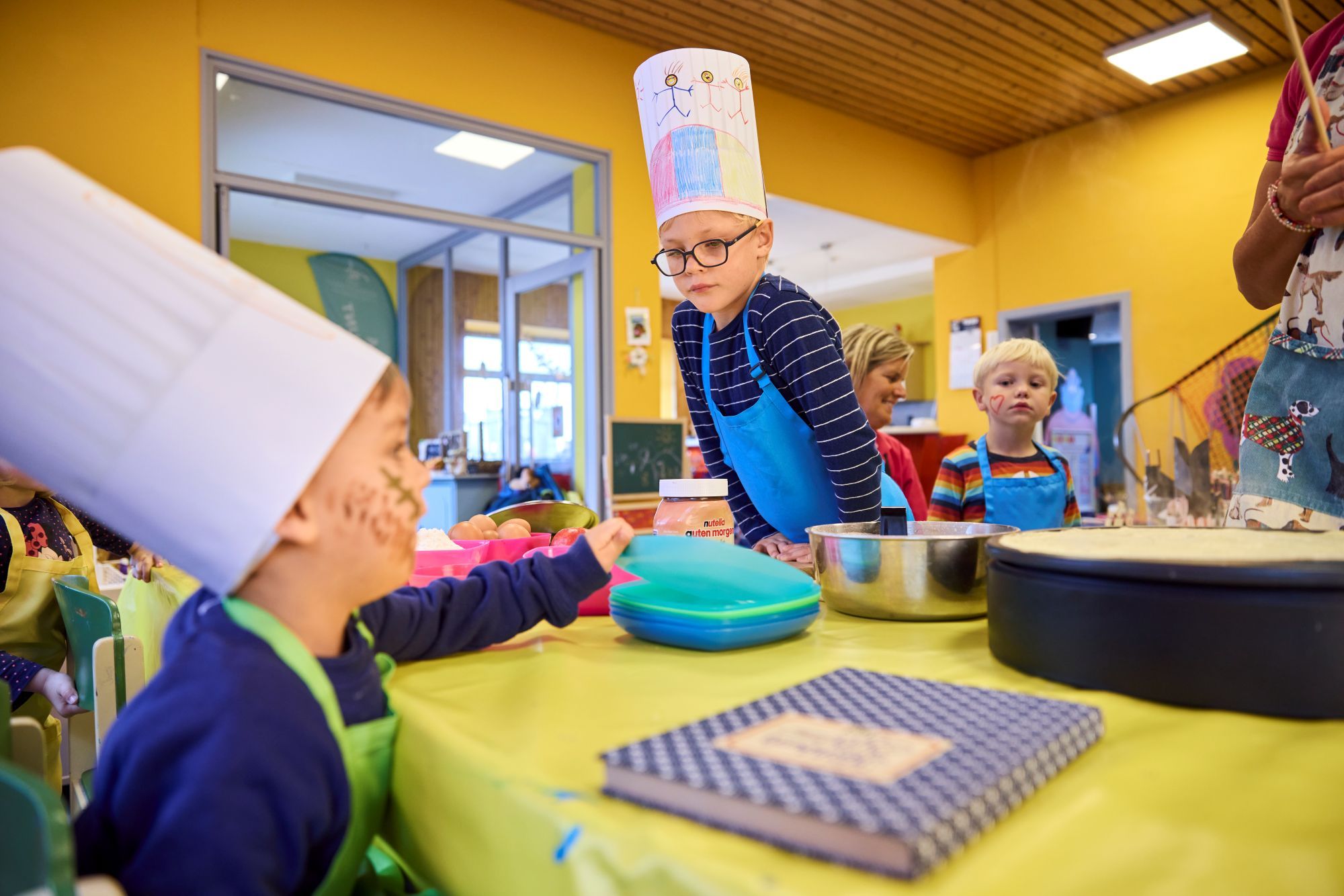 Mehrere Kinder mit Kochhüten aus Papier bei der Backaktion in der Villa Kunterbunt