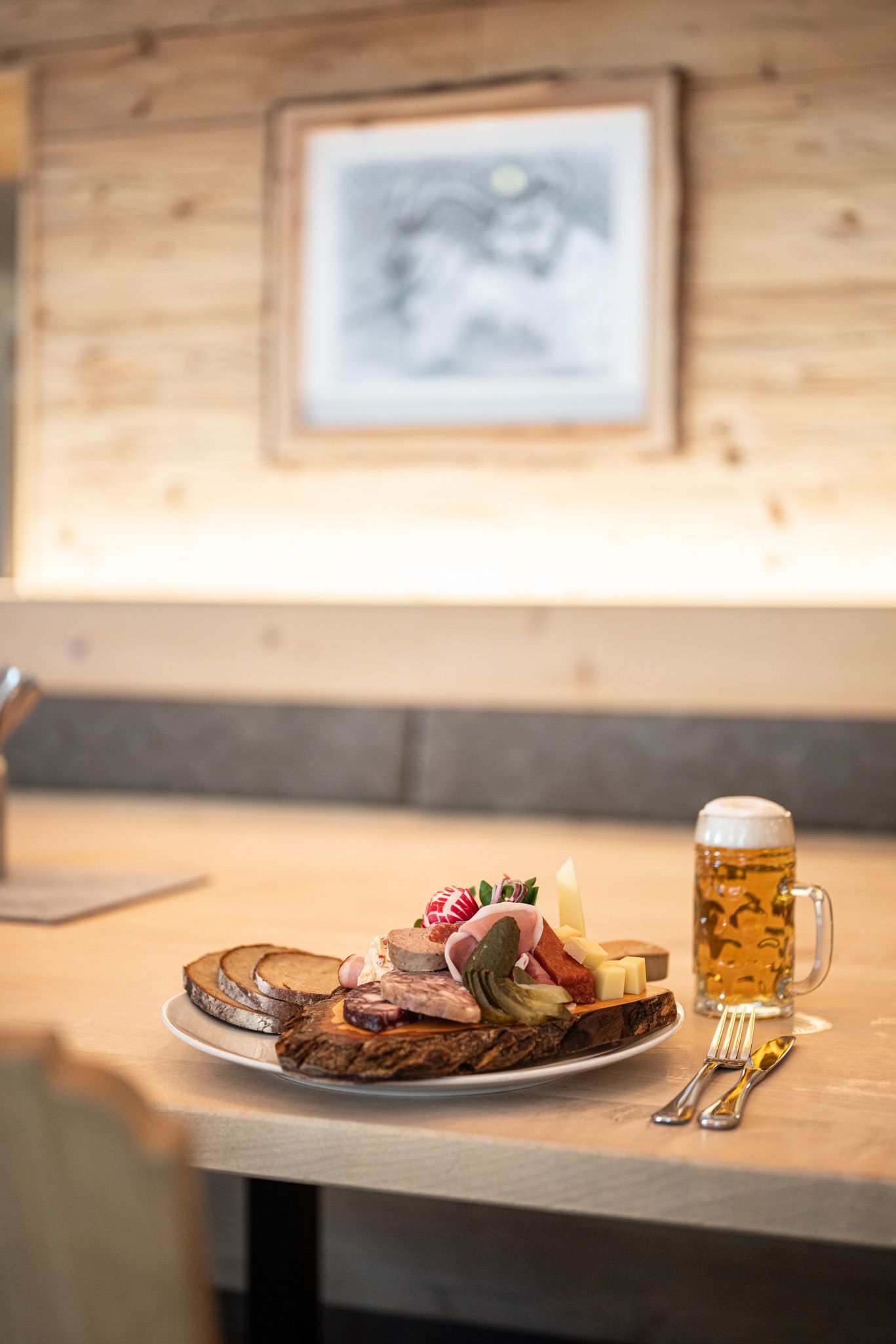 Brotzeit mit Bauernbrot, Käse, Wurst, und Gemüse auf einem Brett, dazu ein frisch gezapftes Bier.