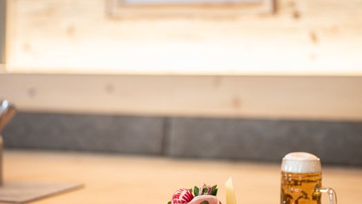 Brotzeit mit Bauernbrot, Käse, Wurst, und Gemüse auf einem Brett, dazu ein frisch gezapftes Bier.