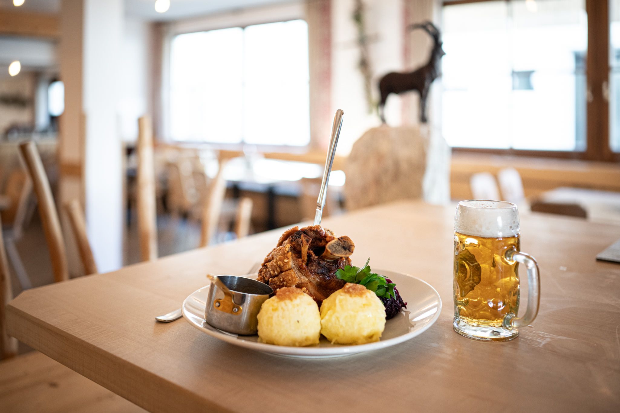 Herzhaft angerichteter Teller mit Knödeln und Schweinehaxe und einem Glas Bier auf einem Tisch im Vordergrund.
