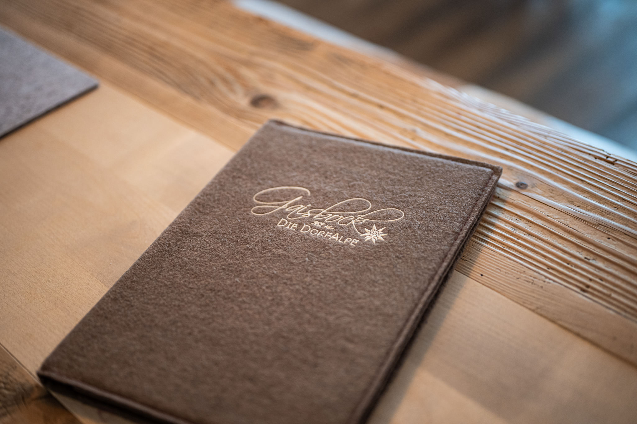 Speisekarte von Gaisbock aus braunem Filz auf einem Holztisch.