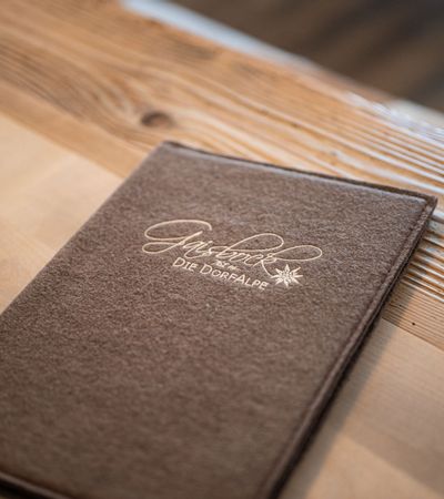 Speisekarte von Gaisbock aus braunem Filz auf einem Holztisch.