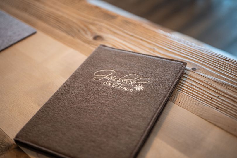 Speisekarte von Gaisbock aus braunem Filz auf einem Holztisch.