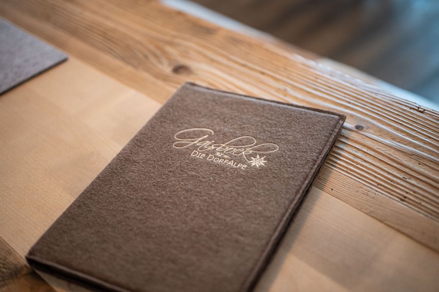 Speisekarte von Gaisbock aus braunem Filz auf einem Holztisch.