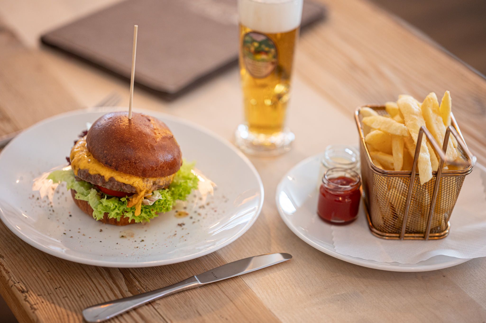 Saftiger Burger mit Pommes, Ketchup und Bier auf einem Holztisch serviert.