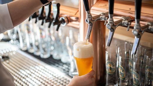 Frisch gezapftes Bier läuft in ein Glas an einer Theke mit mehreren Zapfhähnen.