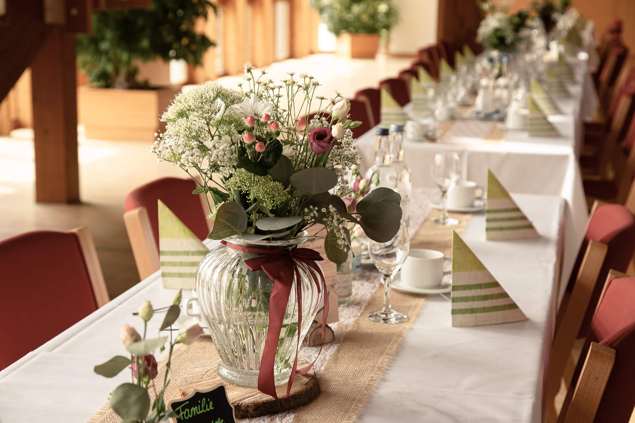 Festlich gedeckte Tafel mit Blumenschmuck in Glasvase, Stoffservietten und gedecktem Geschirr für eine Feier