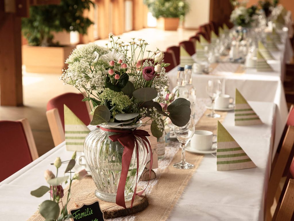 Festlich gedeckte Tafel mit Blumenschmuck in Glasvase, Stoffservietten und gedecktem Geschirr für eine Feier