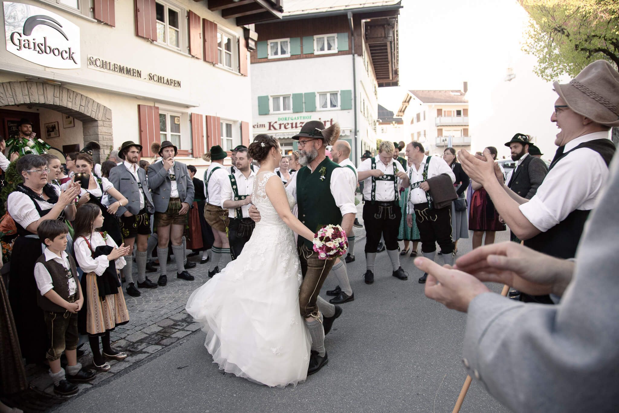 Brautpaar tanzt in Tracht auf der Straße, umgeben von Hochzeitsgästen in traditioneller Kleidung.