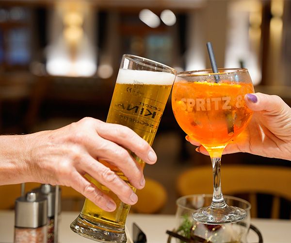 Zwei Gäste stoßen mit einem kühlen Bier und einem spritzigen Aperol Spritz an.