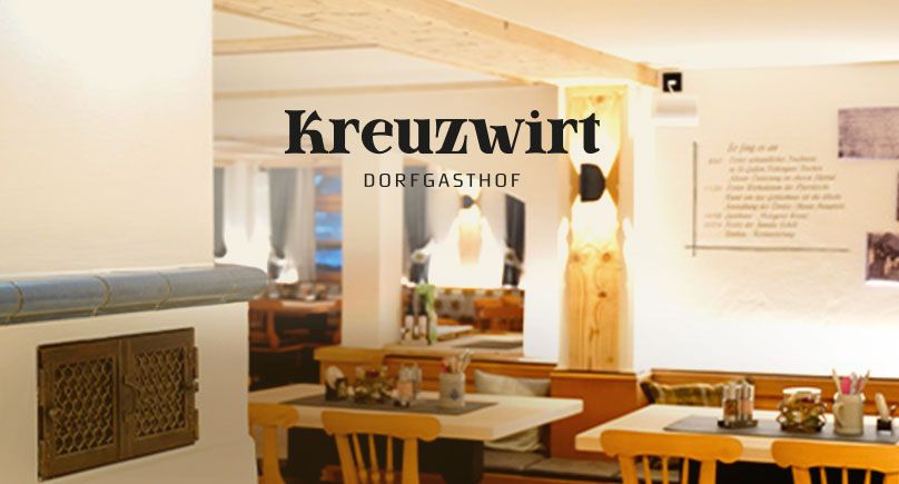 Gemütlicher Gastraum mit Holzinterieur und Kachelofen, im Vordergrund das Kreuzwirt-Dorfgasthof als Gestaltungselement.
