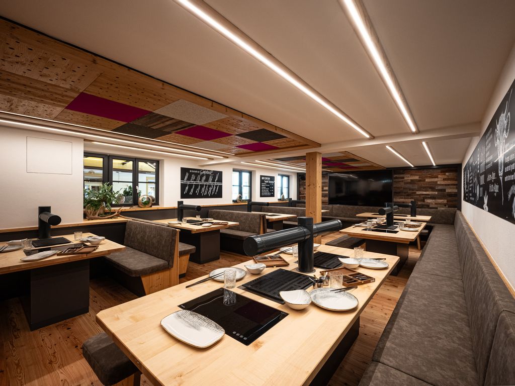 Gemütliche Grillstube mit Holztischen, eingebauten Grills und gepolsterten Sitzbänken in modern-rustikalem Design.