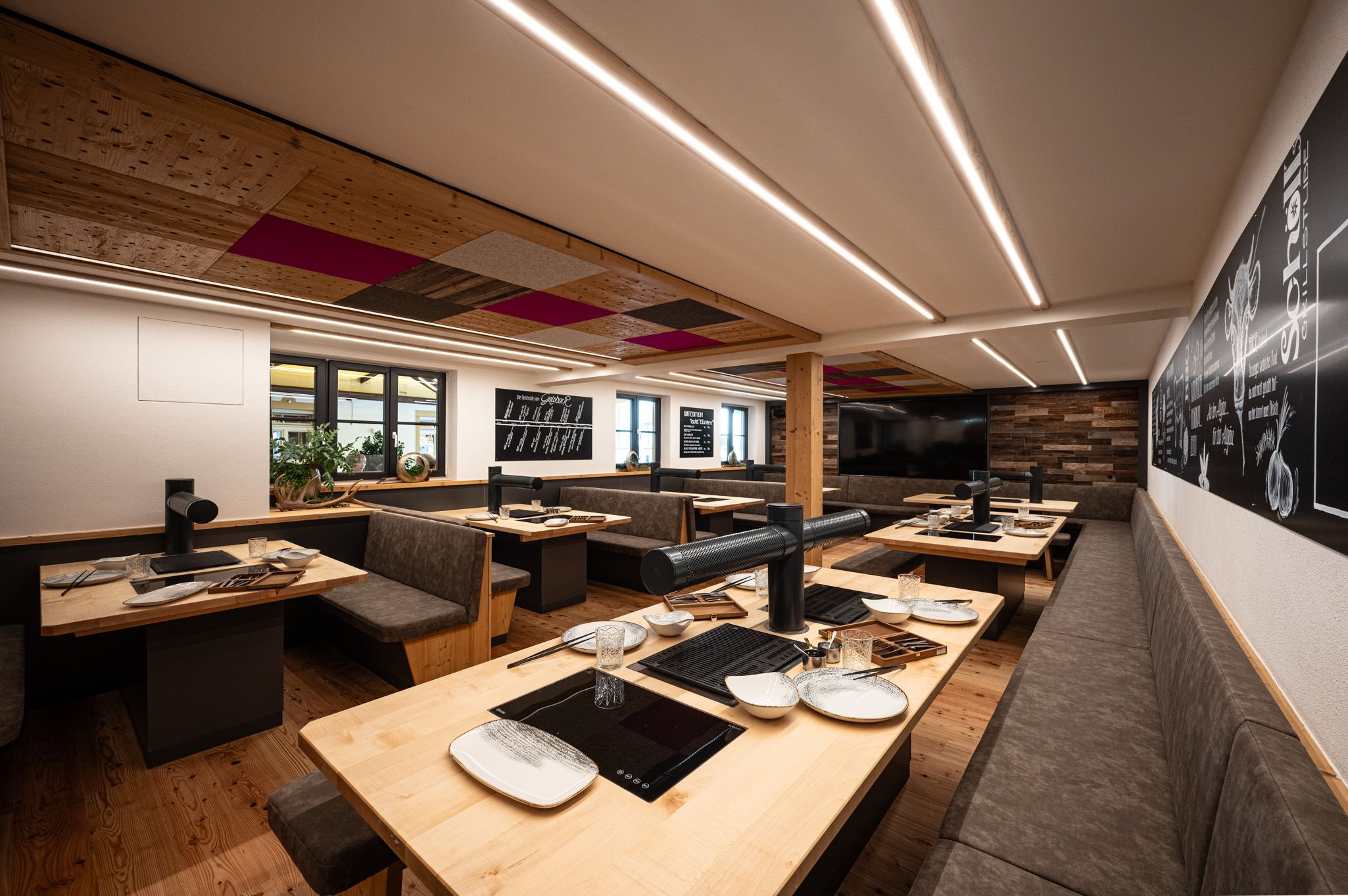 Gemütliche Grillstube mit Holztischen, eingebauten Grills und gepolsterten Sitzbänken in modern-rustikalem Design.