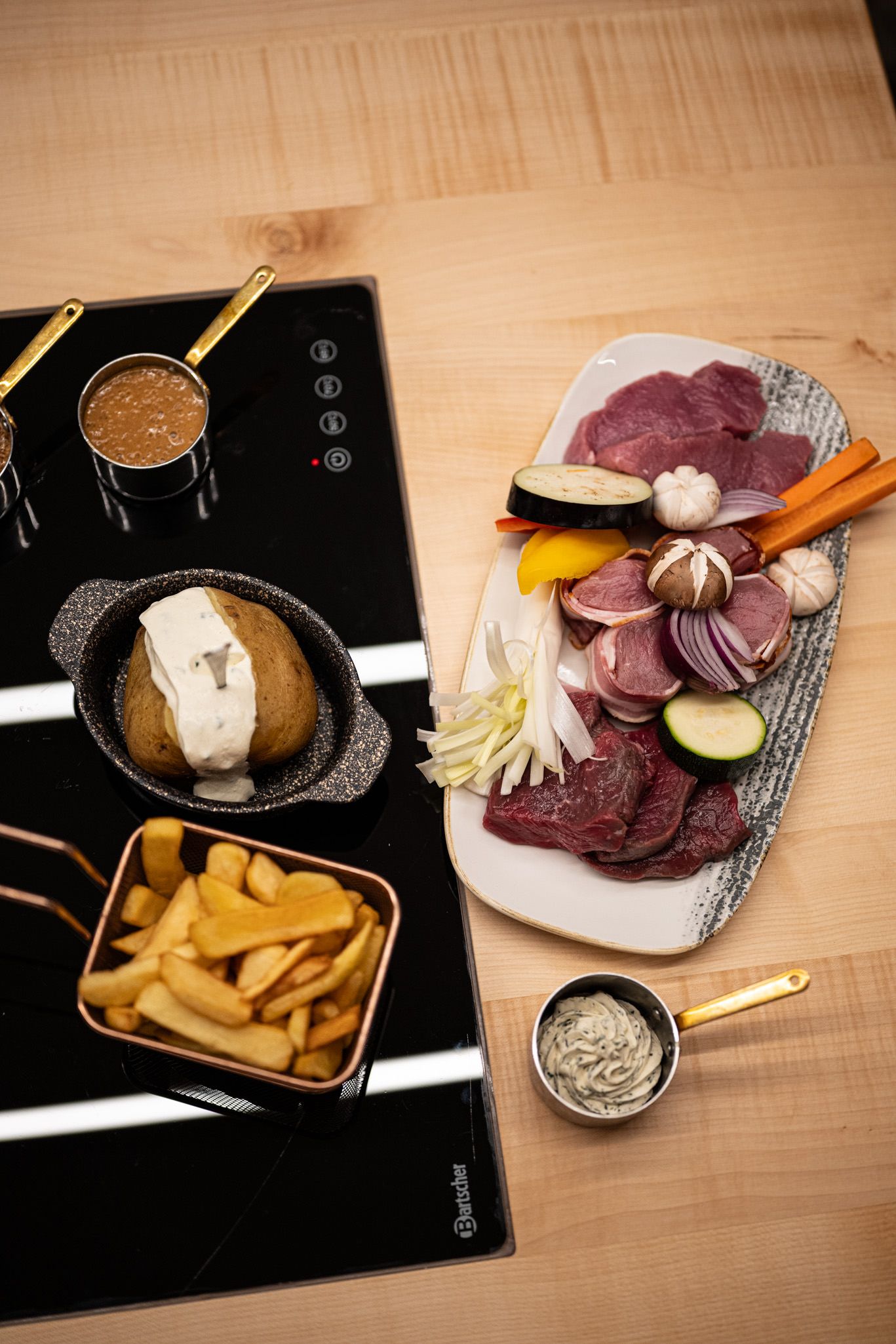 Platte mit frischen Grillzutaten wie Fleisch, Gemüse und Knoblauch, dazu Pommes, Ofenkartoffel und Dips – alles vorbereitet für den Tischgrill in der Grillstube.