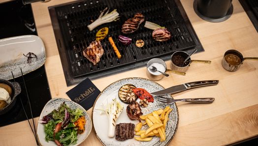 Tischgrill mit gegrilltem Fleisch und Gemüse, dazu ein Teller mit Pommes, Salat und Dips – ein genussvoll angerichtetes Grillgericht in gemütlicher Atmosphäre
